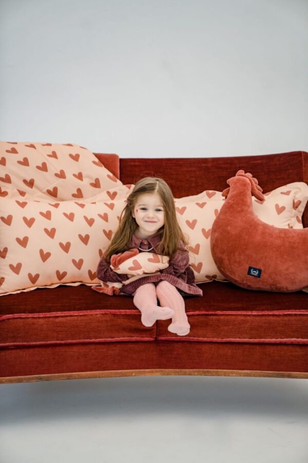Heartbeat Cotto Sleepy Pig Pink, το οποίο κρατάει στο χέρι του ένα παιδάκι με διάφορα προϊόντα της συλλογής Heartbeat γύρω της
